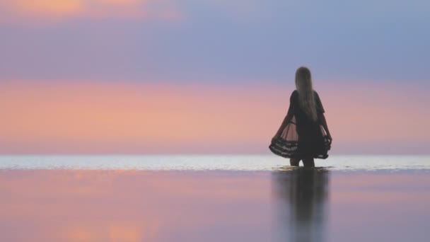 Una ragazza con i capelli biondi chic in bikini nero e uno scialle di pizzo passeggia lungo l'estuario — Video Stock