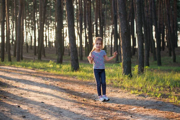 Una chica con el pelo rubio corre a lo largo de un sendero del bosque saltando sobre todas las ramas en la mañana —  Fotos de Stock