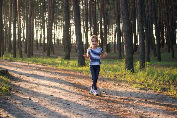 Дівчина зі світлим волоссям біжить по лісовій стежці, стрибаючи над усіма гілками вранці — стокове фото