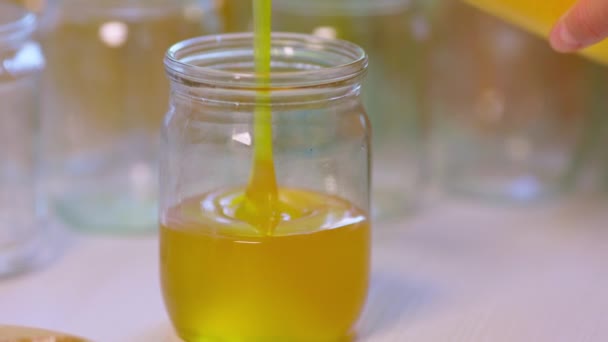 Frau gießt Honig in transparente Gläser auf weißem Tisch — Stockvideo