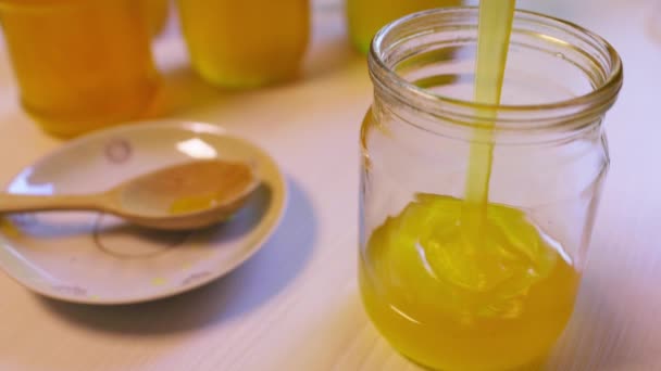 Femme verse du miel dans des pots transparents sur une table blanche — Video