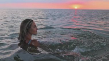 Güzel yüz hatları olan bir kız haliçte otururken bilinmeyen bir mesafeye bakar.