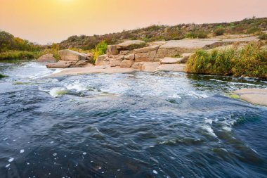 Pürüzsüz ve karanlık taşların arasında küçük parlak bir dere akıyor.