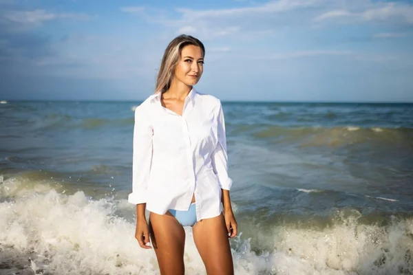 Retrato de uma menina em um maiô azul e camisa branca contra o fundo do mar azul e céu claro — Fotografia de Stock