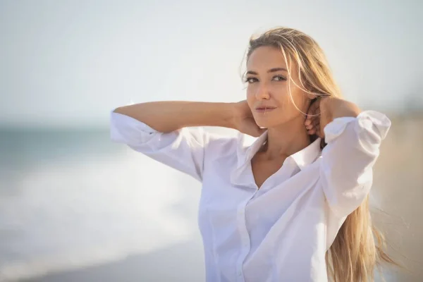 En flicka med långt hår i en blåaktig baddräkt och en skjorta går genom håret på stranden — Stockfoto