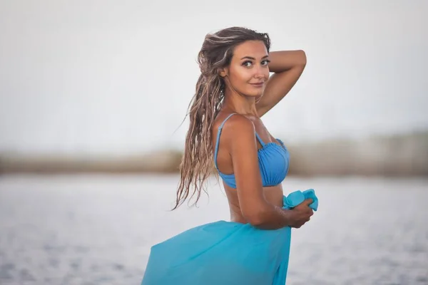 Uma menina com cabelo molhado em um maiô azul e um pareo se saciando ao sol depois de nadar no estuário — Fotografia de Stock