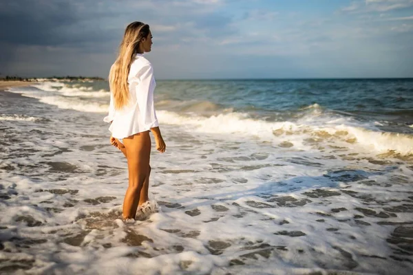 Тонка дівчинка в ніжному блакитному купальнику і сорочці йде по піщаному пляжу біля блакитного моря. — стокове фото