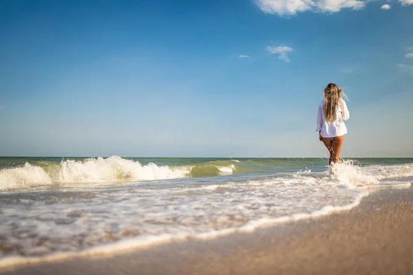 Mavi mayo ve açık renk tişörtlü bronzlaşmış bir kız deniz kenarında yazın tadını çıkarıyor. — Stok fotoğraf
