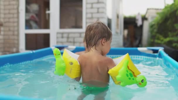 Mom plays with a naked baby in oversleeves in the pool against the background of a summer sunset — Stock Video