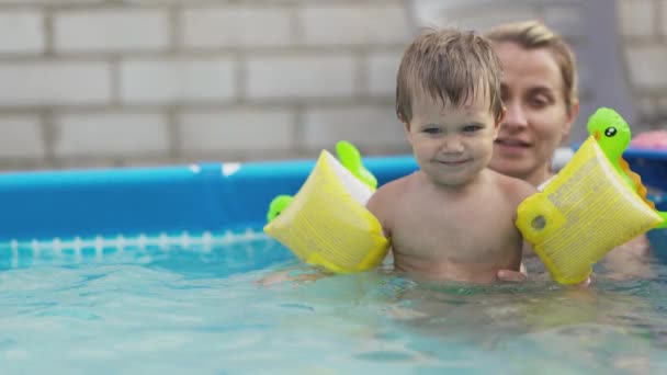 Mama bawi się nagim dzieckiem w podrękawach w basenie na tle letniego zachodu słońca — Wideo stockowe