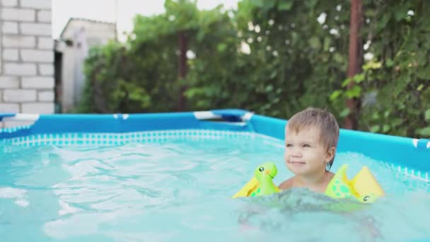 Kind met overmouwen zwemt in het zwembad op de binnenplaats — Stockvideo