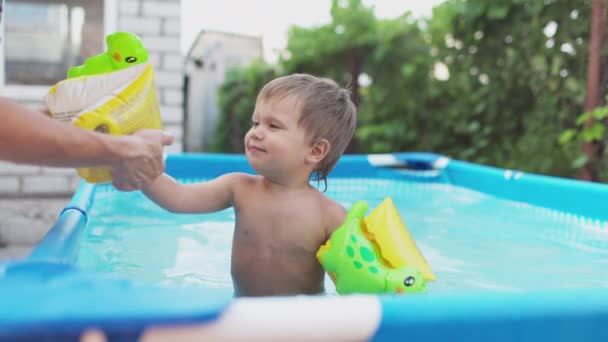 妈妈把袖子套在一个在院子里的游泳池里玩耍的裸体婴儿的胳膊上 — 图库视频影像