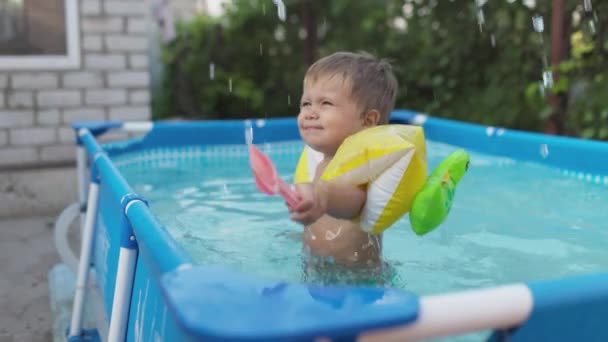 Kind in overmouwen zwemt en plonst in het zwembad in de tuin — Stockvideo