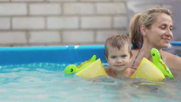 Mãe brinca com um bebê nu em subidas na piscina contra o fundo de um pôr do sol de verão — Vídeo de Stock