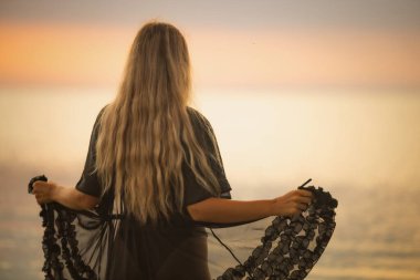 Siyah bikinili, sarı şık saçlı ve dantel şallı bir kız nehir boyunca yürüyor.