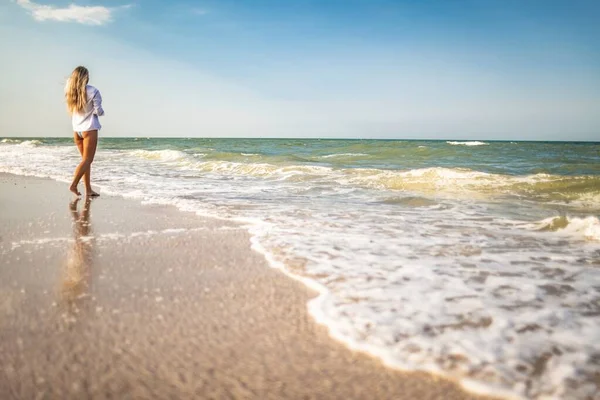 Una chica bronceada en un traje de baño azul y una camisa ligera disfruta del verano en la playa —  Fotos de Stock