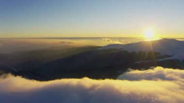 Bulut dalgaları yavaşça kar kaplı dağların tepelerinden akar. Soğuk bir günbatımında ladin ormanlarıyla kaplıdır.