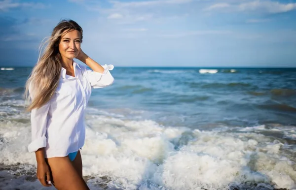 Retrato de uma menina em um maiô azul e camisa branca contra o fundo do mar azul e céu claro — Fotografia de Stock