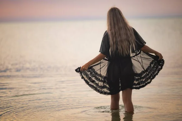 En flicka med blont chic hår i svart bikini och en spets sjal promenader längs flodmynningen — Stockfoto