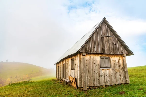 Ένα μοναχικό γκρι σπίτι στέκεται σε ένα υγρό πράσινο λιβάδι ανάμεσα σε πυκνή γκρίζα ομίχλη — Φωτογραφία Αρχείου