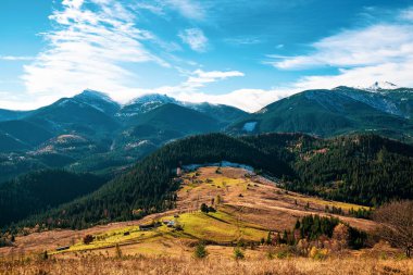 Karpat dağlarını kaplayan güzel renkli ormanlar ve sıcak sonbahar gökyüzünün arka planında küçük bir köy.
