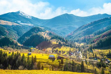 Karpat dağlarını kaplayan güzel renkli ormanlar ve sıcak sonbahar gökyüzünün arka planında küçük bir köy.