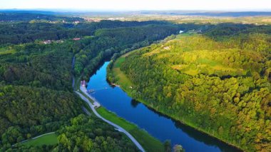 Kupa nehri, Hırvatistan ve Slovenya 'nın yeşil yaprak döken ormanları arasında güneşli bir gökyüzü ve dağların arka planına karşı otoyolun yanında akar. 4K UHD video gerçek zamanlı