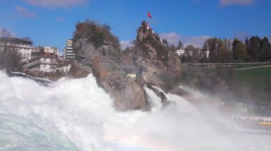 Hızlı fırtınalı soğuk su damlaları düşer ve küçük damlalar Rhine Şelaleleri 'ne İsviçre' deki eski kasabanın arka planına doğru farklı yönlere dağılır. 4k video yavaş çekim UHD