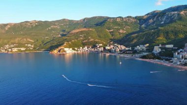 Budva ve Becici tatil beldeleri, sakin Adriyatik Denizi yakınlarında lüks oteller ve rahat plajlarla Karadağ Dağları ve mavi gökyüzüne karşı. UHD Video gerçek zamanlı 4K