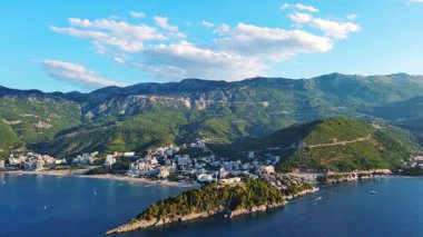 Budva ve Becici tatil beldeleri, sakin Adriyatik Denizi yakınlarında lüks oteller ve rahat plajlarla Karadağ Dağları ve mavi gökyüzüne karşı. UHD Video gerçek zamanlı 4K