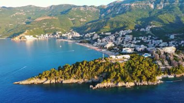Budva ve Becici tatil beldeleri, sakin Adriyatik Denizi yakınlarında lüks oteller ve rahat plajlarla Karadağ Dağları ve mavi gökyüzüne karşı. UHD Video gerçek zamanlı 4K