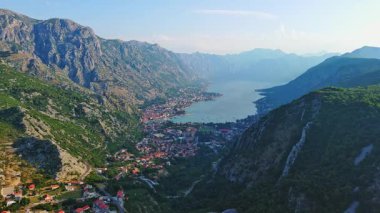 Deniz ünlü Kotor Koyu tatil köyü plajları ve otelleri, açık mavi güneşli gökyüzünün zeminine karşı Karadağ dağlarının gölgesindeki gök mavisi Adriyatik Denizi. UHD Video gerçek zamanlı 4K