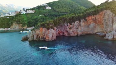 Gezintiler için küçük beyaz bir motorlu tekne yüksek tehlikeli uçurum yamaçlarının altında turkuaz deniz suyunda yüzüyor. UHD Video gerçek zamanlı 4K