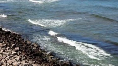 Bulgaristan 'ın parlak güneşli günbatımı ışığı altında, Karadeniz' in yansıtıcı ilkbaharı yakınlarında, koyu nemli deniz kumları ve büyük ıslak kayalık kayalıkları olan vahşi bir taş ve kumlu bir sahil. HD yavaş çekim videosu