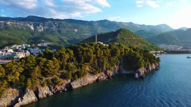 Adriyatik Denizi kıyılarında bitki örtüsü bulunan tarihi antik St. Nicholas adası kıyı kentleri, Karadağ dağları ve açık gökyüzü karşısında yer alıyor. UHD Video gerçek zamanlı 4K
