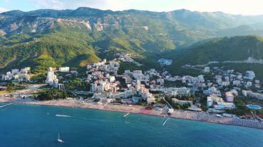 Budva ve Becici tatil beldeleri, sakin Adriyatik Denizi yakınlarında lüks oteller ve rahat plajlarla Karadağ Dağları ve mavi gökyüzüne karşı. UHD Video gerçek zamanlı 4K