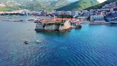 Küçük gemileri ve tekneleri olan deniz turizm limanı antik tarihi Budva adası yakınlarındaki Adriyatik Denizi 'nde romantik bulutlu gökyüzüne karşı. UHD Video gerçek zamanlı 4K