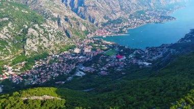 Deniz ünlü Kotor Koyu tatil köyü plajları ve otelleri, açık mavi güneşli gökyüzünün zeminine karşı Karadağ dağlarının gölgesindeki gök mavisi Adriyatik Denizi. UHD Video gerçek zamanlı 4K