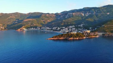 Budva ve Becici tatil beldeleri, sakin Adriyatik Denizi yakınlarında lüks oteller ve rahat plajlarla Karadağ Dağları ve mavi gökyüzüne karşı. UHD Video gerçek zamanlı 4K