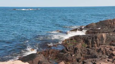 Bulgaristan 'ın parlak güneşli günbatımı ışığı altında, Karadeniz' in yansıtıcı ilkbaharı yakınlarında, koyu nemli deniz kumları ve büyük ıslak kayalık kayalıkları olan vahşi bir taş ve kumlu bir sahil. 4K UHD yavaş çekim videosu