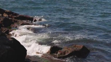 Bulgaristan 'ın parlak güneşli günbatımı ışığı altında, Karadeniz' in yansıtıcı ilkbaharı yakınlarında, koyu nemli deniz kumları ve büyük ıslak kayalık kayalıkları olan vahşi bir taş ve kumlu bir sahil. 4K UHD yavaş çekim videosu