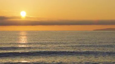 Calm blue boundless Black Sea with cool water reflecting light and sandy wild empty beach nearby, against cloudy colored sky with white clouds and bright dawn sun. UHD 4K video timelaps