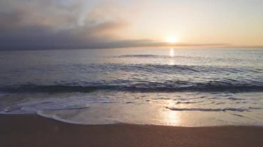 Calm blue boundless Black Sea with cool water reflecting light and sandy wild empty beach nearby, against cloudy colored sky with white clouds and bright dawn sun. UHD 4K video timelaps
