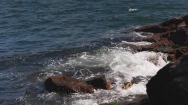 Bulgaristan 'ın parlak güneşli günbatımı ışığı altında, Karadeniz' in yansıtıcı ilkbaharı yakınlarında, koyu nemli deniz kumları ve büyük ıslak kayalık kayalıkları olan vahşi bir taş ve kumlu bir sahil. 4K UHD yavaş çekim videosu