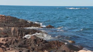 Bulgaristan 'ın parlak güneşli günbatımı ışığı altında, Karadeniz' in yansıtıcı ilkbaharı yakınlarında, koyu nemli deniz kumları ve büyük ıslak kayalık kayalıkları olan vahşi bir taş ve kumlu bir sahil. 4K UHD yavaş çekim videosu