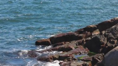 Bulgaristan 'ın parlak güneşli günbatımı ışığı altında, Karadeniz' in yansıtıcı ilkbaharı yakınlarında, koyu nemli deniz kumları ve büyük ıslak kayalık kayalıkları olan vahşi bir taş ve kumlu bir sahil. 4K UHD yavaş çekim videosu