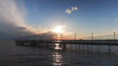 Sakin ve sakin bir Karadeniz 'de, bulutlu, çok renkli bir gökyüzü ve parlak bir akşam günbatımına karşı eski, boş, küçük bir rıhtımın yan görüntüsü. 4K UHD yavaş çekim videosu