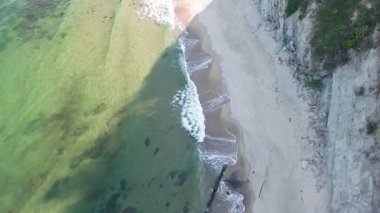 A wild empty sandy beach between a rocky sharp large ledge, covered with green fresh new vegetation, and a deep calm cool Black Sea under a clear blue sky. UHD 4K video realtime