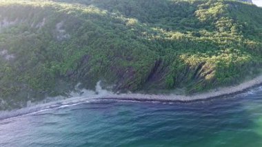 A wild empty sandy beach between a rocky sharp large ledge, covered with green fresh new vegetation, and a deep calm cool Black Sea under a clear blue sky. UHD 4K video realtime