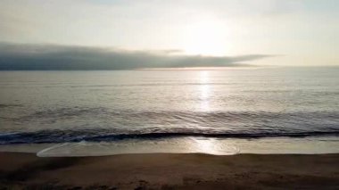Sakin mavi uçsuz bucaksız Karadeniz, ışığı yansıtan soğuk su ve yakındaki kumlu boş kumsal, bulutlu renkli gökyüzüne karşı beyaz bulutlar ve parlak şafak güneşi. UHD 4K video gerçek zamanlı